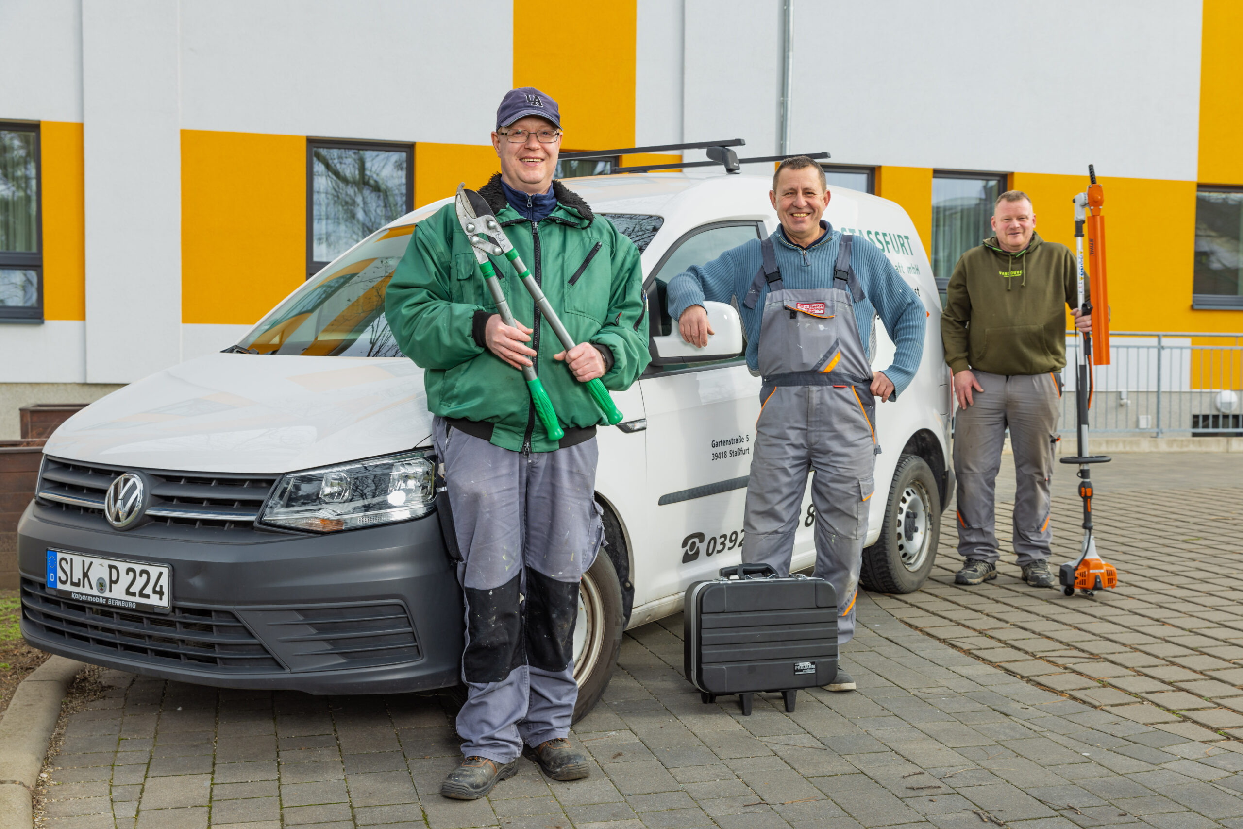 F-Hausmeister-2801 Männer in Arbeitskleidung vor einem Auto